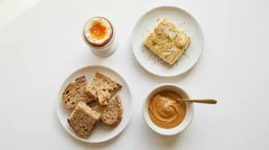 Alimentos alergênicos introdução alimentar — ovo, pasta de amendoim, peixe e trigo sobre superfície branca com luz natural